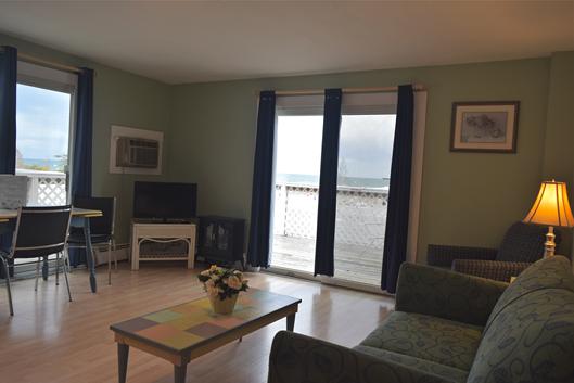 A wide view of a living room with a sofa, coffee table, TV, and dining table, with sliding doors leading to a balcony with a view.