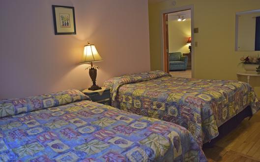 A hotel room with two beds, a nightstand, and a lamp.