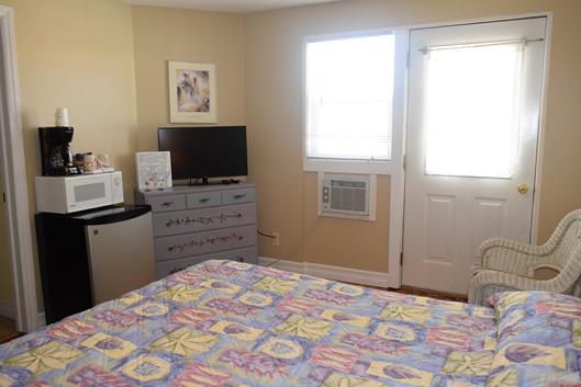 A wide view of a hotel room with a bed, TV, microwave, coffee maker, and refrigerator.