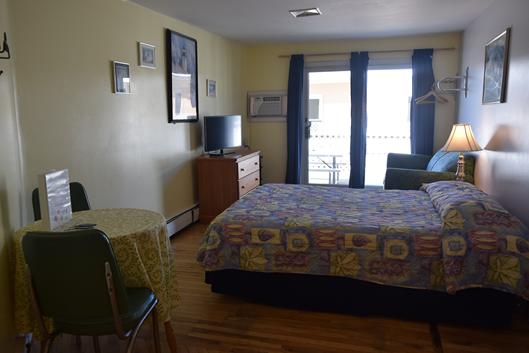 A wide-angle view of a hotel room with a bed, desk, and TV.